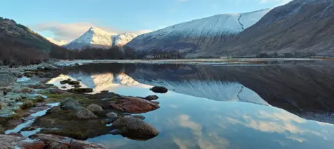 Fiona Berry A body of clear water, with hills in the background reflected in the water