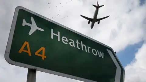 Getty Images Plane flies over a road sign for Heathrow Airport