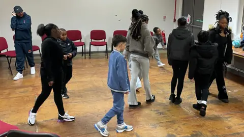 Children walk around a hall trying to avoid each other as part of a drama session