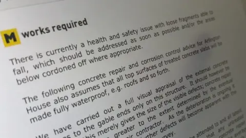 A close-up of a printed report showing text under the heading "works required". The document refers to a health and safety issue involving loose fragments that could fall and recommends repairs and further assessment of a concrete structure.