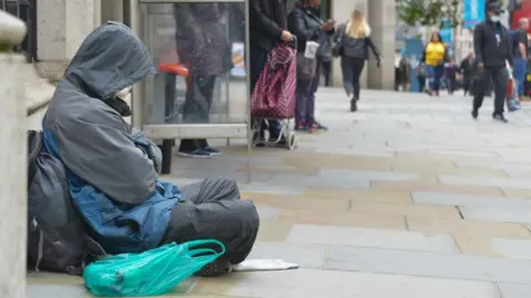Getty Images File image showing a person wearing a grey coat and trousers sleeping by a bus stop on a street near Charing Cross Station 