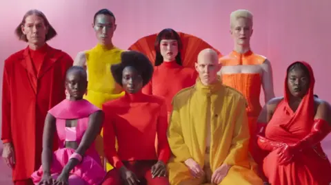 Models in bright coloured clothes sit facing the camera and posing for an advert for Jaguar cars