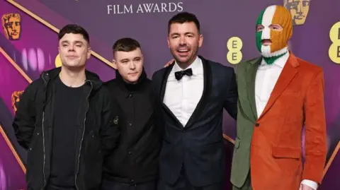 Getty Images Mo Chara aka Naoise O Caireallain, Moglai Bap aka Liam Og O Hannaidh, Rich Peppiatt and DJ Provai of Kneecap - one is in a green, white and orange suit and balaclava