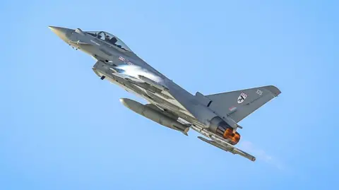 British Royal Air Force Eurofighter Typhoon jet flies upwards into a clear blue sky.
