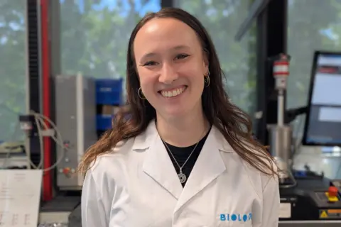 A woman in a lab coat smiles at the camera