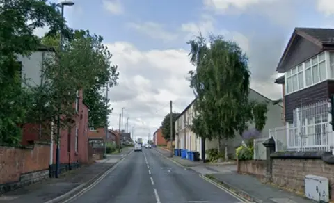 Google Street view. Houses with blue and grey wheelie bines outside line a grey-coloured roadway.