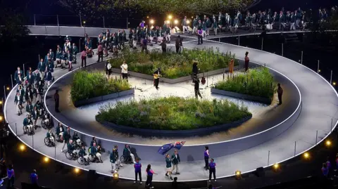 Getty Images Athletes walking out at the Commonwealth Games opening ceremony, making their way around a circular stage set, with a garden in the middle of it.