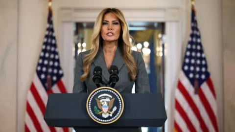 Alex Wong via Getty Images US First Lady Melania Trump in a grey suit speaks from the White House 