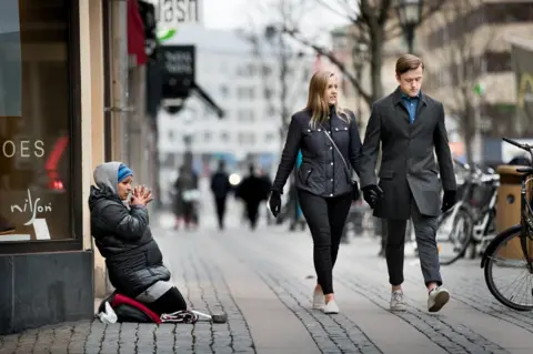 Kicki Nilsson A woman begs as a smart couple walks past.