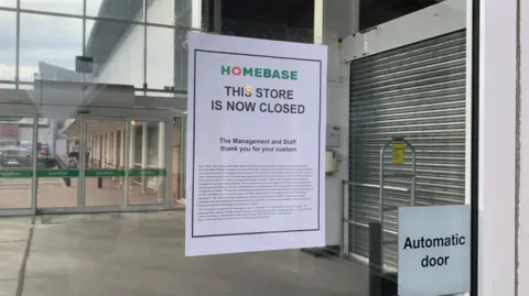 A sign on a glass sliding automatic door informs customers that the Homebase store is now closed