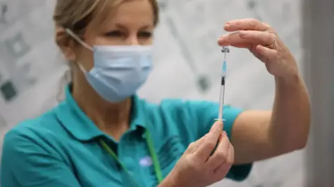 A woman is wearing a blue mask while holding a syringe.