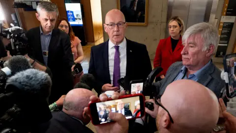 PA Media First Minister John Swinney speaks to the media in the Scottish Parliament