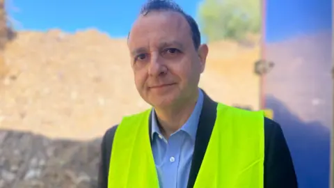 Alberto Costa is wearing a high-vis jacket and a suit. 