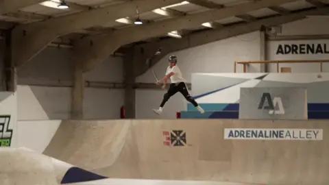 Jayden Sharman in the middle of the air performing a scooting trick at Adrenaline Alley.