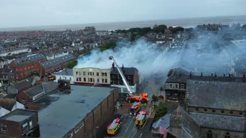 Kevin Haworth Drone aerial image of a fire on Lord Street, Fleetwood, as firefighters tackle the blaze. There are three fire engines and an aerial platform at the scene. Smoke is seen billowing from the roof of the three-storey building.