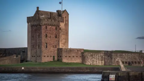 A large castle set in front of the River Tay with grass surrounding the front of the building