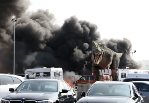 A model dinosaur stood in frozen roar as smoke billowed into the sky behind it 