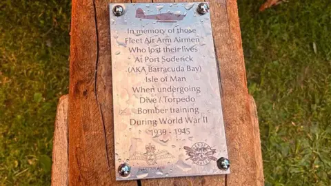 A close up of a plaque on the bench which reads "In memory of those Fleet Air Arm Airmen who lost their lives at Port Soderick (AKA Barracuda Bay) Isle of Man when undergoing dive/torpedo bomber training during World War II.