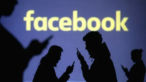 Reuters Silhouettes of mobile users next to a screen projection of the Facebook logo, 28 March 2018