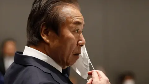 Getty Images Haruyuki Takahashi, executive board member for the Tokyo Organising Committee of the Olympic and Paralympic Games (Tokyo 2020), puts on a face mask during a Tokyo 2020 executive board meeting on the COVID-19 coronavirus outbreak in Tokyo on March 30, 2020.