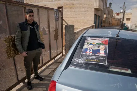 BBC Abdel Wadi stands next to a poster of his relatives Ibrahim and Ahmed Wadi, who were killed last week