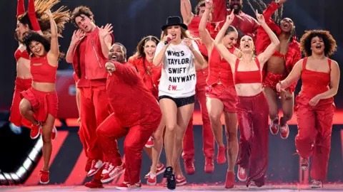 Getty Images Taylor Swift in a "Who's Taylor Swift anyway?" t-shirt with dancers dressed in red outfits