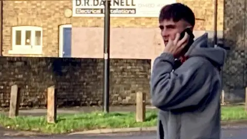 A man wearing a grey hooded top holding a mobile phone to his left ear with his left hand.