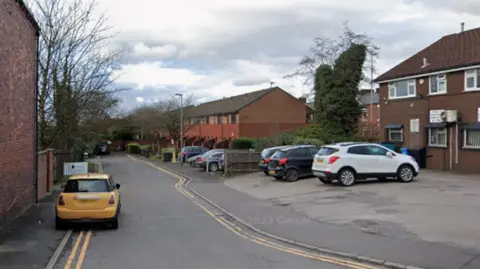 A yellow mini, parked on double yellow lines, at the entrance to Plumpton Close with houses on the right