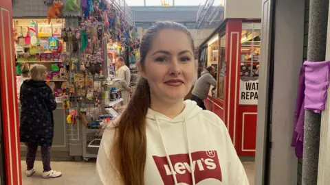 A young woman with dark, long hair and wearing a cream hooded top with a red Levi logo