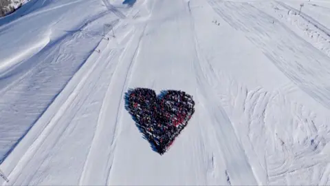 Aerial view of skiers in the shape of a heart on a ski slope