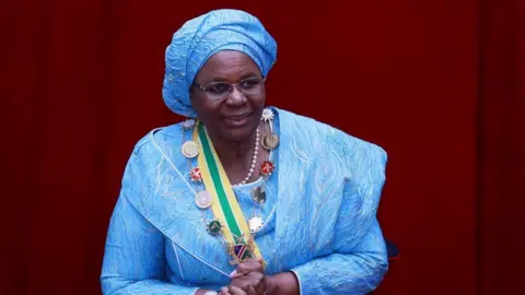 Reuters Namibia's first female President, Netumbo Nandi-Ndaitwah, wearing a blue dress and headwrap, has her hands clasped together during her inauguration in Namibia. 