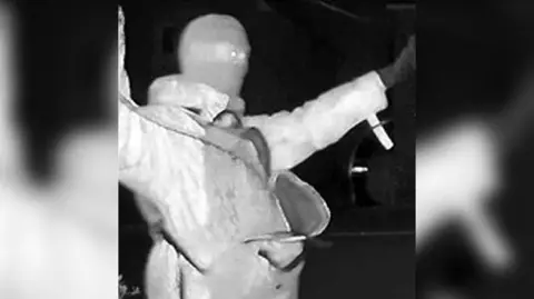 Nottinghamshire Police A man wearing a balaclava is shown on CCTV footage, he has his arms spread out wide.