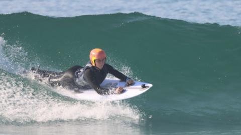 Hannah Dines para surfing, wearing wet suit and pink helmet. 
