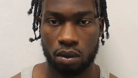 Met Police Martin Asolo-Ogugua police mugshot. He is looking at the camera and is wearing a light grey vest.