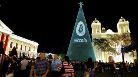 People gather around a Christmas tree light installation displaying a Bitcoin logo in El Salvador's capital, San Salvador.