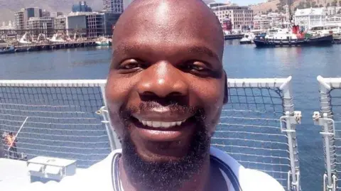 A smiling Sibusiso Aserie Ndlovu is seen in a white T-shirt