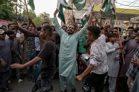 AKRAM SHAHID/AFP via Getty Images Pakistani people celebrate after the ceasefire. Men are seen with their hands in the air and waving flags