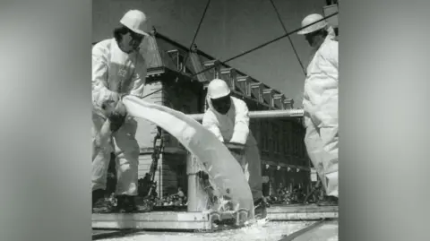 Three men pour batter through tubes. The picture is black and white.
