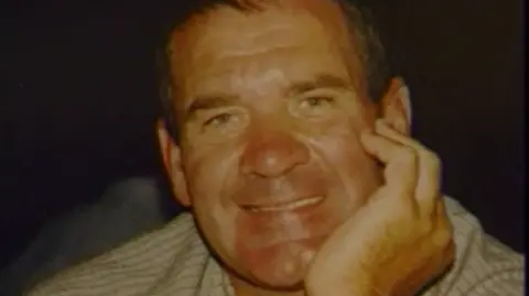 Michael Steele smiling and leaning on his hand. He is wearing a white shirt with fine black stripes.