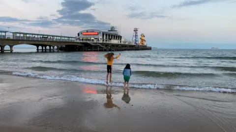 Two girls in the foreground, splashing in the sea next to Bournemouth pier