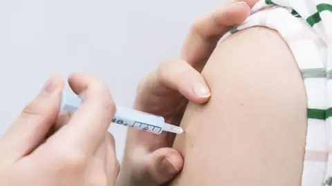 An image of a person getting vaccinated. The vaccines is being injected into a person's arm. 