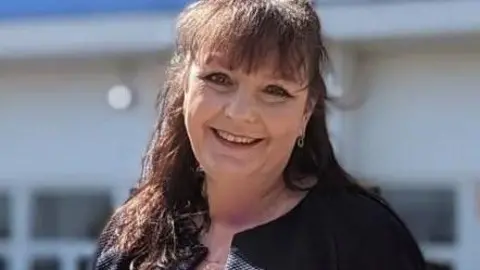 Chief nursing officer Natalie Green standing in front of a hospital building. She has long hair, which is partly tied back, and she is wearing a black top.