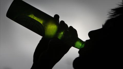 Generic image of a man in shadow drinking from a botte of beer