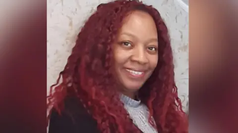 Faye Delaney Faye Delaney has dyed, long dark red hair and is wearing a grey top under a black top. She is smiling at the camera.