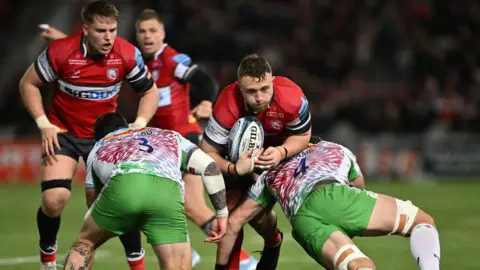 Ruan Ackermann of Gloucester is tackled by Simon Kerrod and Dino Lamb of Harlequins