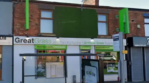 Exterior shot of the front of Great Grass in Oldham. It is next to a bus stop on a shopping street in Oldham.