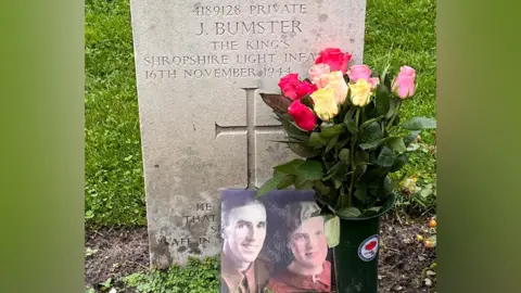 Family photograph A picture of James Bumster's grave in Venray, the Netherlands. There is a photograph of him and his wife on the grave, along with pink and white roses.