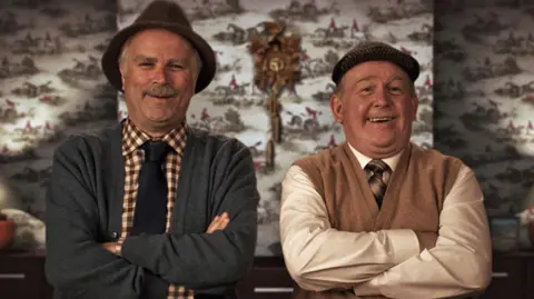 Victor and Jack from Still Game smile at the camera with their arms folded