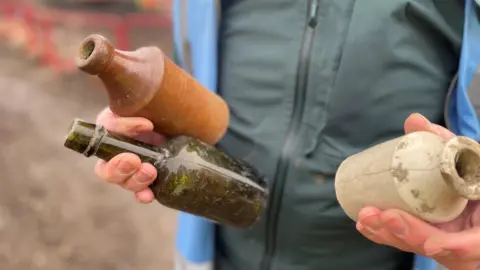 Photo shows a man's torso and hands holding three ancient vases