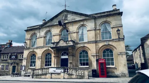 Corsham Town Hall is a historical building with large windows and a red telephone box outside of it. 